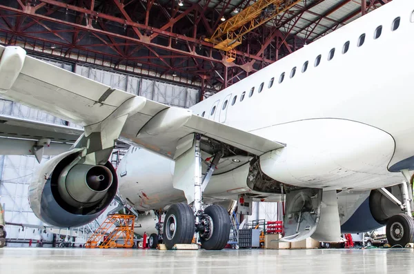 Passenger aircraft on maintenance of engine and fuselage repair in airport hangar. Rear view, under the wing