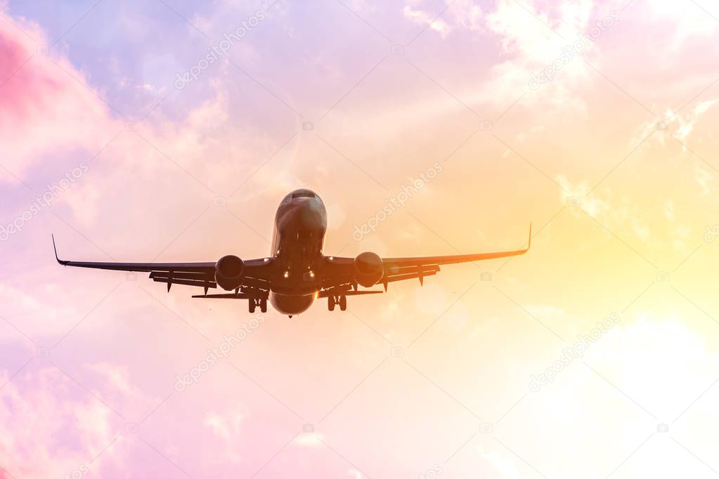 Airplane silhouette in warm in the yellow-pink tones of the sky and clouds. Copcept travel to warmer countries.