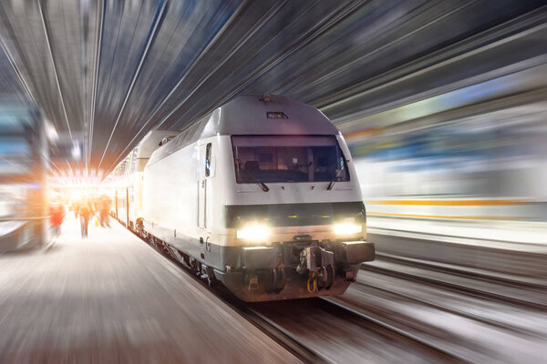 Поезд едет на высокой скорости на вокзале в ночном городе
.