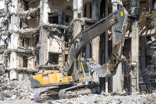 As ruínas de um edifício demolido desmoronaram, pilhas de pedras e poeira. Escavadeira funciona com balde . — Fotografia de Stock