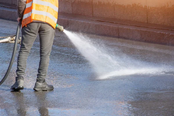 Worker cleaning driveway with gasoline high pressure washer splashing the dirt, asphalt road. High pressure cleaning.