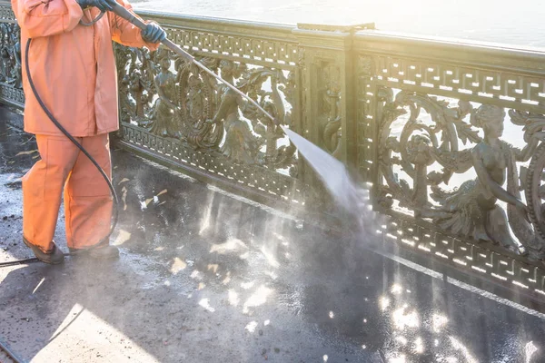 Worker cleaning driveway with gasoline high pressure washer splashing the dirt, railings, bumpers bridge. High pressure cleaning.