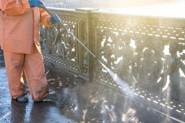 Worker cleaning driveway with gasoline high pressure washer splashing the dirt, railings, bumpers bridge. High pressure cleaning.