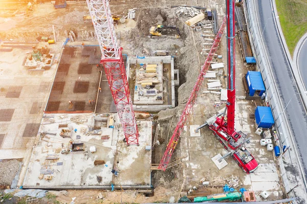 Aerial view, crane truck at the construction site works the installation of the boom of a tower crane, against the background of the foundation of the building under construction.