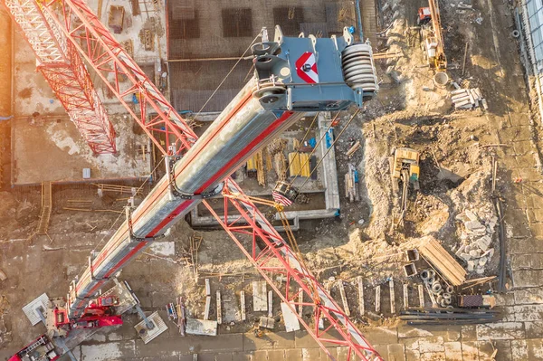 Aerial view, crane truck at the construction site works the installation of the boom of a tower crane, against the background of the foundation of the building under construction.