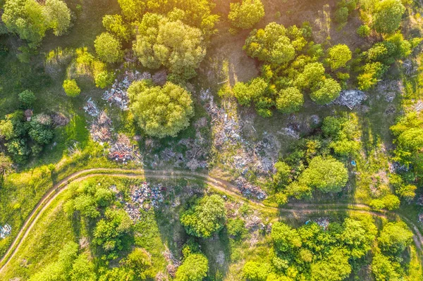 Large landfill of garbage, household waste, plastics and other things among the green forest along the meadows and the road. Aerial view from above drone. — Stock Photo, Image