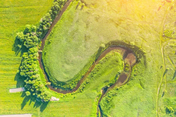 Légi táj vidéken a kanyargós kis folyó, patak zöld mezőben, felülnézet naplemente rét. — Stock Fotó