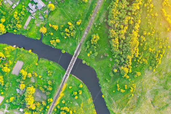 Railway bridge among green meadows over a small river in the countryside, aerial view