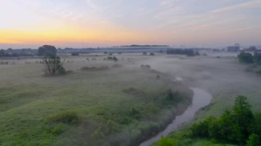 Kırsal alanlarda çimenli çayırlar arasında küçük bir nehir üzerinde güzel sis, şafak vakti erken saatlerde.