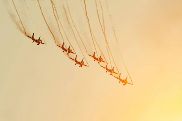 黒い煙の痕跡と白い蒸気渦雲の痕跡を持つオレンジ色の空の戦闘機のグループ. — ストック写真