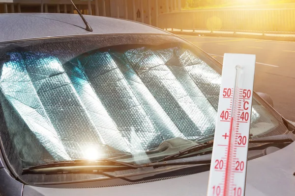 Beschermend reflecterend oppervlak onder de voorruit van de personenwagen geparkeerd op een warme dag, verwarmd door de zonnestralen. De thermometer toont de temperatuur in de auto. — Stockfoto