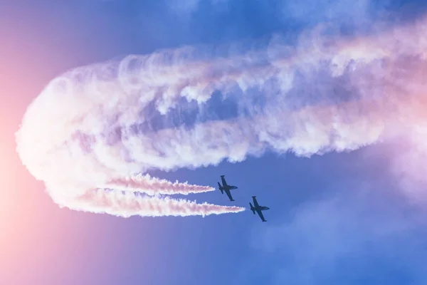 Un par de aviones de combate volando contra un cielo brillante, realizando figuras se convierte del humo . — Foto de Stock