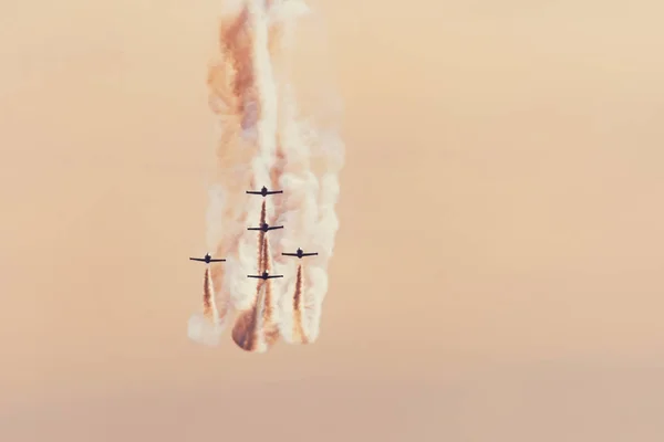 Groep van gevechtsvliegtuigen vliegtuigen vliegen tegen een heldere oranje hemel, het uitvoeren van figuren uit de Smoke Trail. — Stockfoto