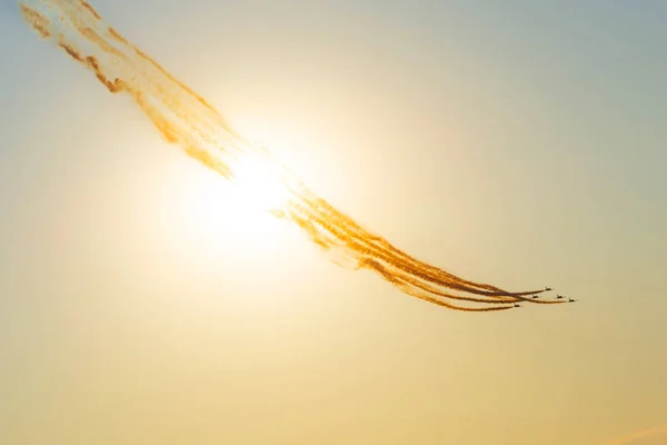 夕暮れ時の夕方の太陽と黄色とオレンジの空を通るエアプレーンと煙の道. — ストック写真