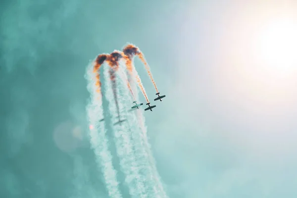 Drei leichte Triebwerke führen Kunstflug aus. die helle Sonne erhellt die Flugzeuge und die Schatten fallen auf den Rauch, den sie am Himmel hinterlassen. — Stockfoto