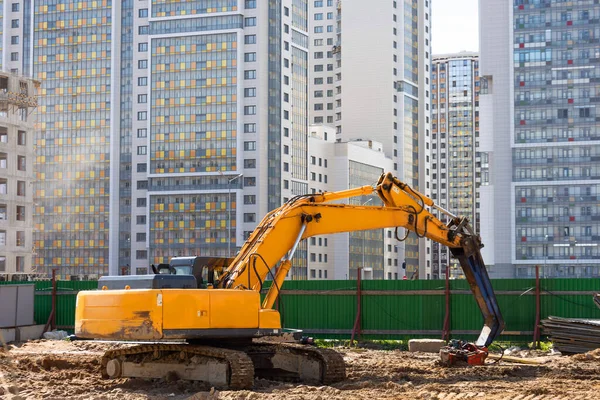 Heavy excavator in a working high frequency hydraulic vibratory mounted pile driver on road against the background of residential multi-storey buildings
