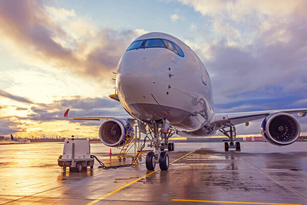View of an airplane parked at an airport during sunset bright light shine and clouds in the sky
