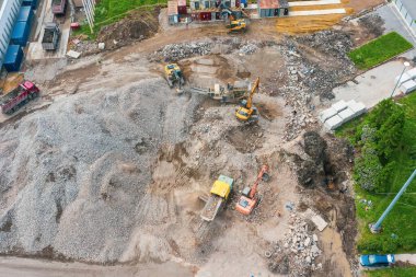 Yıkılmış bir binanın şantiyesinde çalışan kazıcılar. Çimento kalıntılarını ezici ekipmanlara yüklüyorlar ve toprağı taşıyorlar.