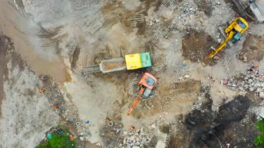 Yıkılmış bir binanın şantiyesinde çalışan kazıcılar. Ezici ekipmanlara çimento yükleme ve toprak öğütme taşları, hava üst görünümü