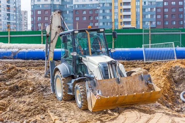 在建造起重机和多层建筑物的过程中 一辆装有桶的拖拉机停在建筑工地 — 图库照片