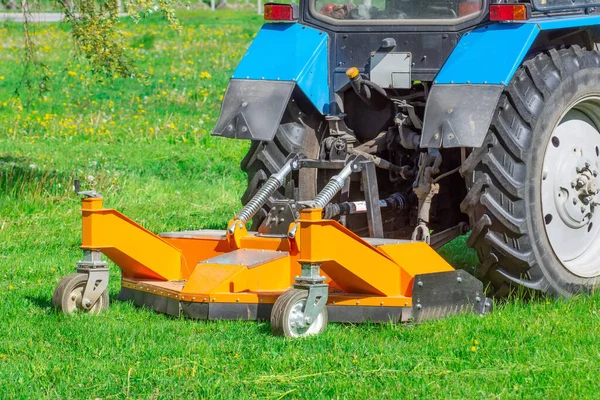 トラクターは都市の芝生に草を刈るためにトレイル芝刈り機を使用しています バックビュー — ストック写真