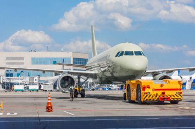 Uçak bakımı için özel ekipman kullanarak bir yolcu uçağını çekmek. Terminal binasının arka planında kalkış uçuşu