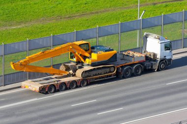 Şehirdeki otobanda uzun bir karavan platformu olan nakliye kamyonunda uzun sarı kazı alanı var.