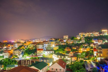 Deniz kenarında bir sürü evi olan tatil köyü manzarası dağlarda gece ışıkları.