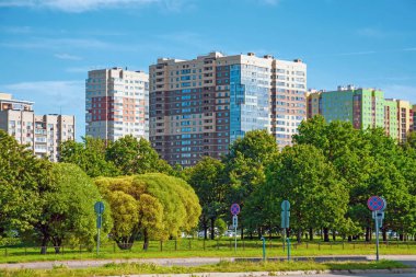 Genç meşeler ve söğütlerle dolu yeşil yaz parkı. Arka planda, çok katlı binalar nüfus için ekolojik olarak temiz bir alan.