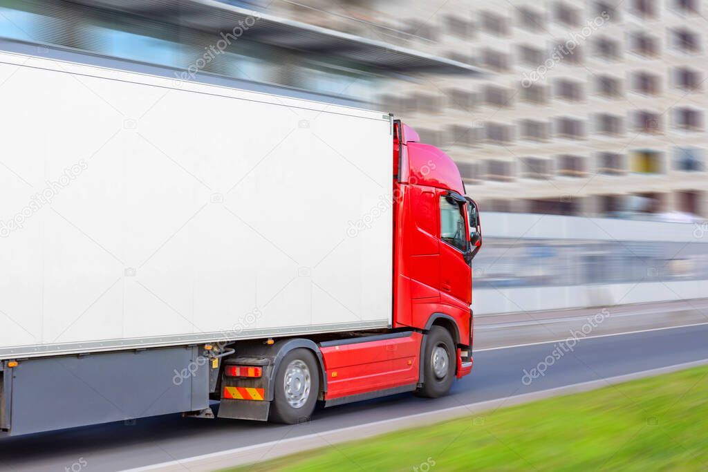 Red truck on blurry asphalt road over blue cloudy sky background