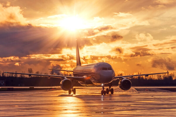 Sunset view of airplane on airport runway under dramatic sky with bright light sunshine after the evening rain