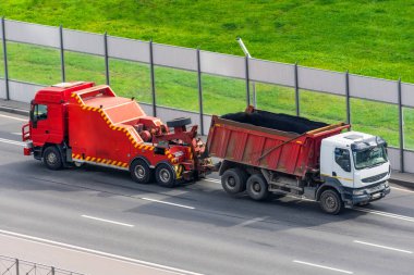 Güçlü büyük kamyon yarı tahliye çekici çekicileri ve eklenmiş kırık tahliyeli kamyonla birlikte şehir otobanında araba sürüyor.