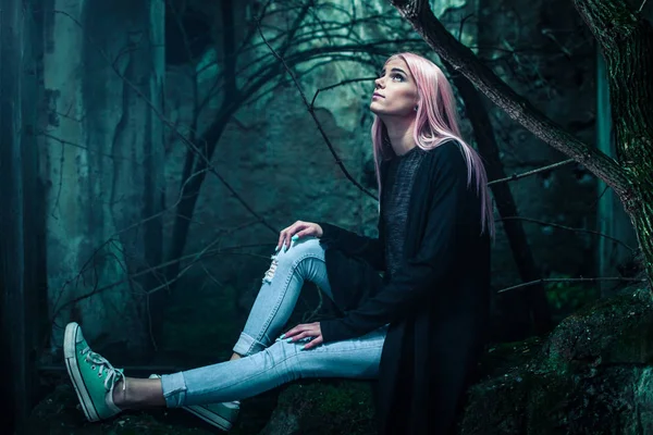 年轻迷人的女人的照片粉红色的头发和穿孔坐在石头在黑暗的森林 — 图库照片