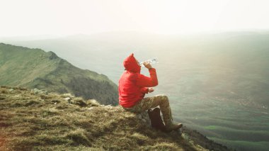 Kırmızı ceketli taş dağları içki suda açık oturan genç adam fotoğrafı