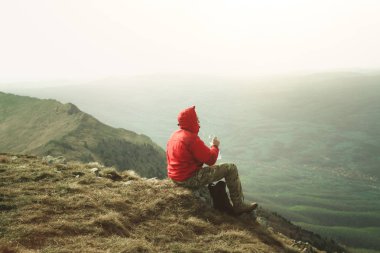 Kırmızı ceketli taş dağları içki suda açık oturan genç adam fotoğrafı