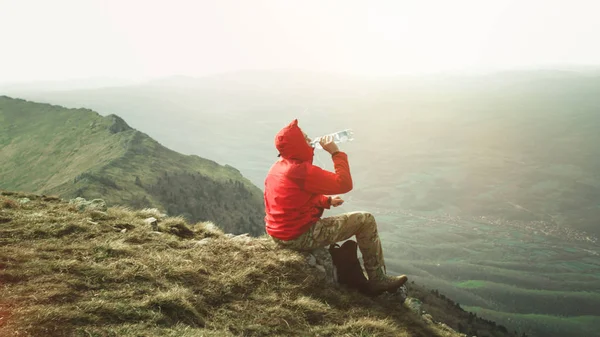 Kırmızı ceketli taş dağları içki suda açık oturan genç adam fotoğrafı