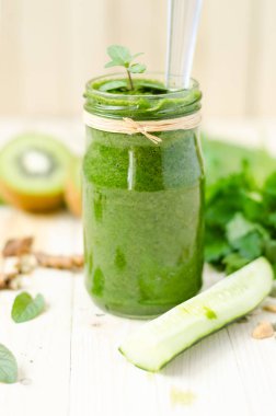 Ispanak, kivi ve turuncu ışık ahşap masa retro bir kavanoza sağlıklı yeşil yüzlü. Salatalık ön planda, kivi içinde belgili tanımlık geçmiş.