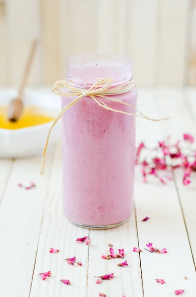 Pink Strawberry Smoothie in retro jar with purple flowers and honey on light rustic boards.