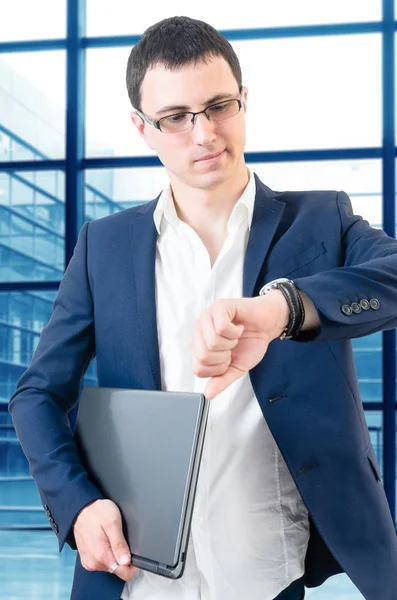 年轻的商人戴着眼镜 手里拿着手提电脑在机场看手表 — 图库照片