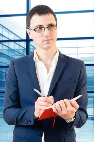 Young businessman wearing glasses and waiting for plane on the airport with the note in his hand