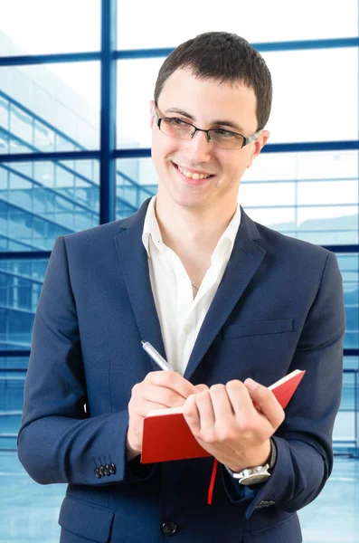 Young business man taking notes for the next meeting looking happy over big office's windows background