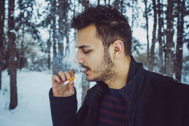 Genç çekici adam ormanda kar fırtınası sırasında sigara