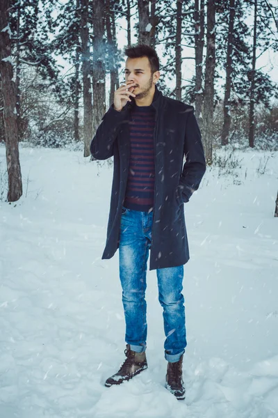 雪灾期间年轻迷人的男子在森林里抽烟 — 图库照片
