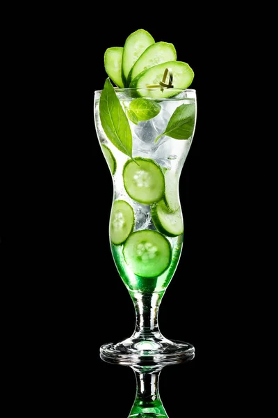 Green cocktail with cucumber in glass in front of black background