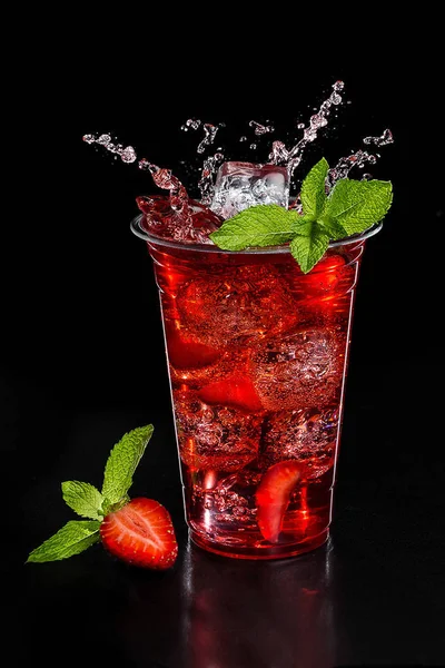Red cocktail in glass with ice and mint front of black background