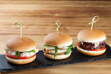 Ahşap arka planda üç hamburger, Vejetaryen, balık, sığır pirzola