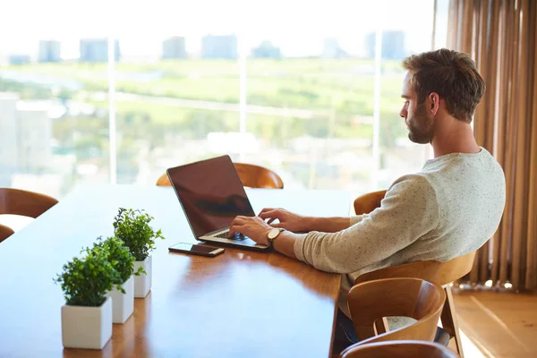 Moderner Mann sitzt am Esstisch und arbeitet mit seinem Laptop — Stockfoto