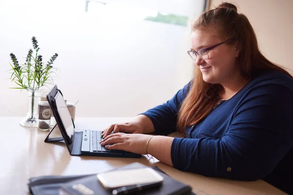 Plus-Size-Frau tippt in hellem Café auf Tablet Stockbild