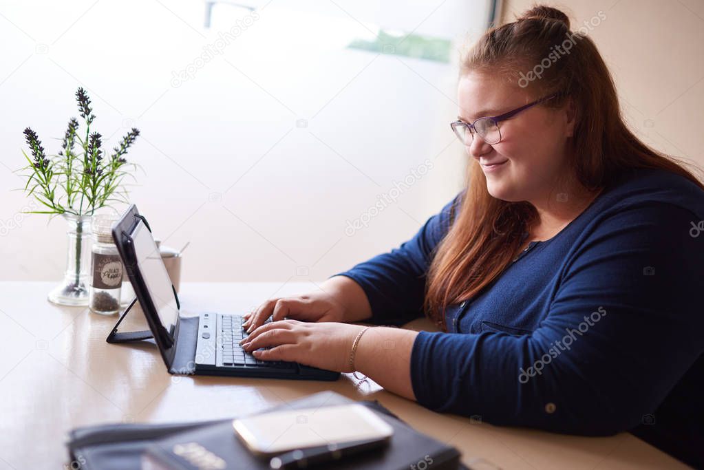 plus size woman typing on tablet in a bright cafe