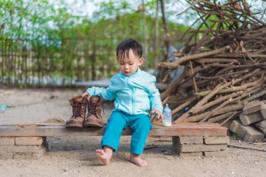 Asyalı bebek şişeden süt içerken baba botu giymeye çalışıyor.